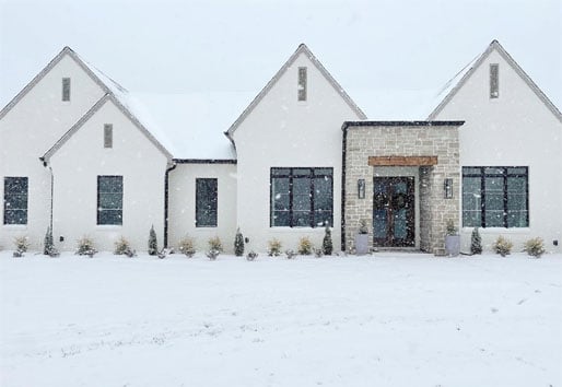 A white home with new black windows is snug against the snowy, cold landscape outside.