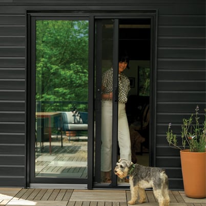 A woman pulls a retractable insect screen across the opening side of her Andersen 200 Series Narroline Gliding Patio Door.
