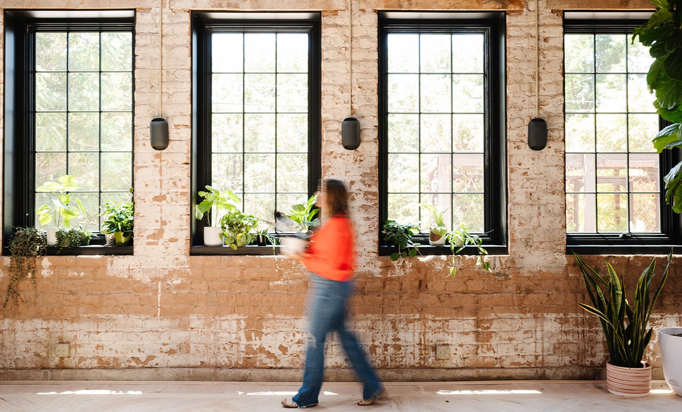 An exposed brick wall punctuated by four Andersen® A-Series Casement Windows with black frames and a 3-over-5 colonial grille pattern.