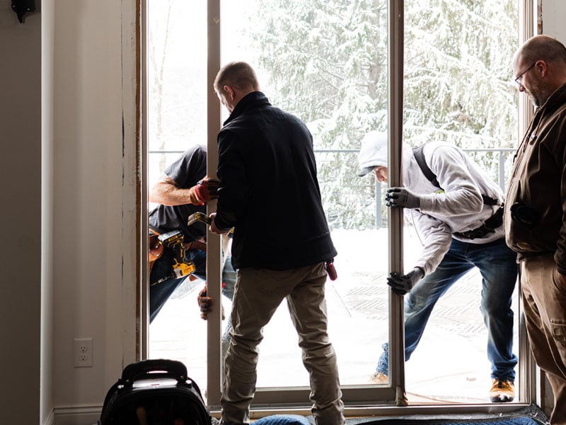 Contractors work to remove an old patio door in preparation for installing a new one.