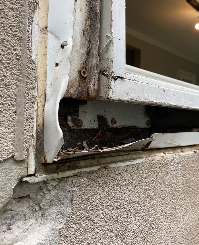 another angle of the window, where the frame and surrounding stucco are improperly sealed. There are gaps and cracks visible between the frame and the stucco, which suggest further vulnerability to moisture. The wear and tear are apparent, and the window seems to lack proper caulking or flashing to prevent water ingress.