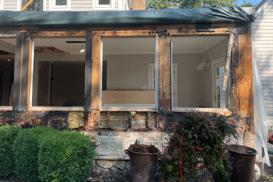 4 window rough openings in a house undergoing significant repairs or renovation. The house appears to have experienced some severe water damage related to poor window installation. The exterior wall shows exposed wooden framing and parts of the house are stripped down to the structural layers. The area near the windows is particularly affected, with missing or damaged material around the window frames.