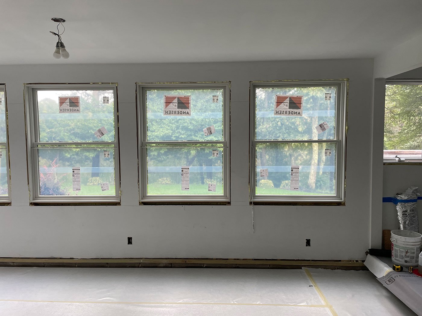 a room with three side-by-side windows installed. The windows appear to be intact and in place, with views of the outside through them. Inside the room, the windows are set within a finished wall, and the surrounding interior looks clean and complete. Sunlight is coming through the windows, highlighting the room’s bright and well-lit atmosphere.