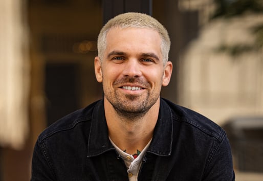 A headshot of Tyler Grace sitting on a bench wearing a black jean jacket.