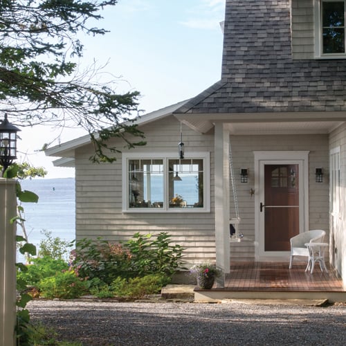 A retractable screen storm door on a summer cottage with woods in the foreground and lake in the background.