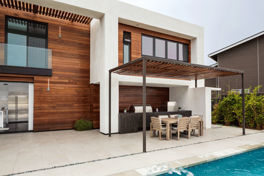 A modern home with a combination of stucco and wood siding and large black windows looks out onto a pool.