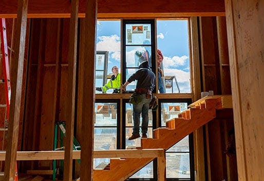 Three people work together to install a window in a new construction home.