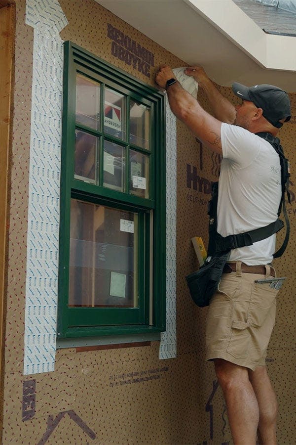 A person adds flashing around a window.